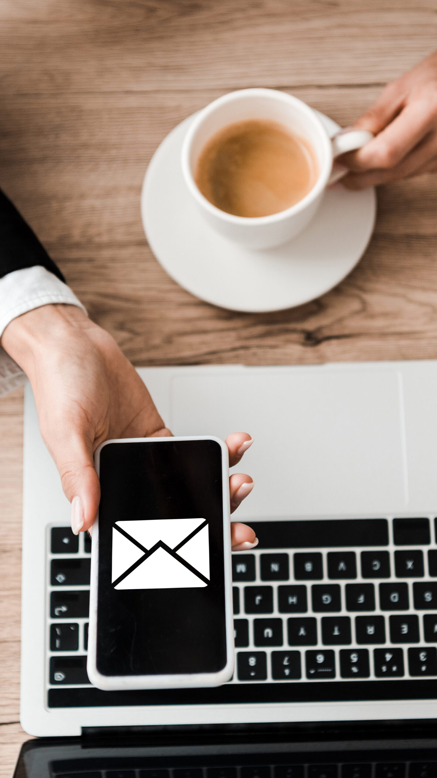 top view of businesswoman holding smartphone with envelope on screen and cup with coffee near laptop